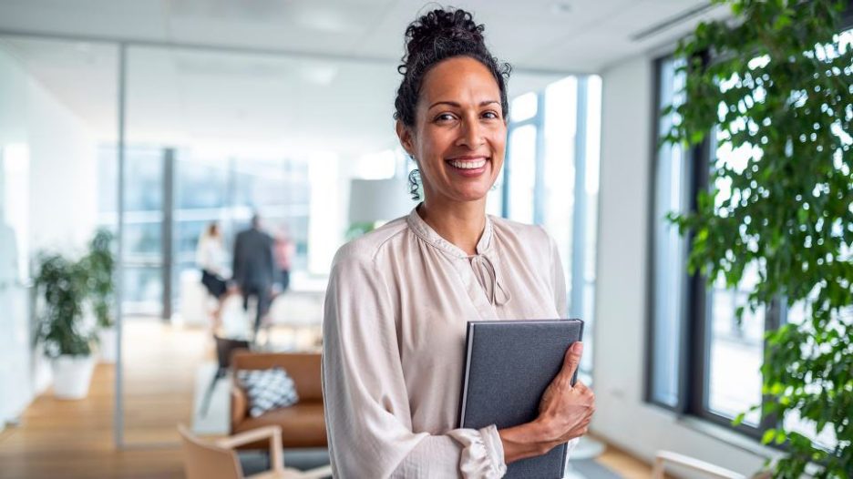 Female profesional standing in office holding notebook while smiling and looking at camera 